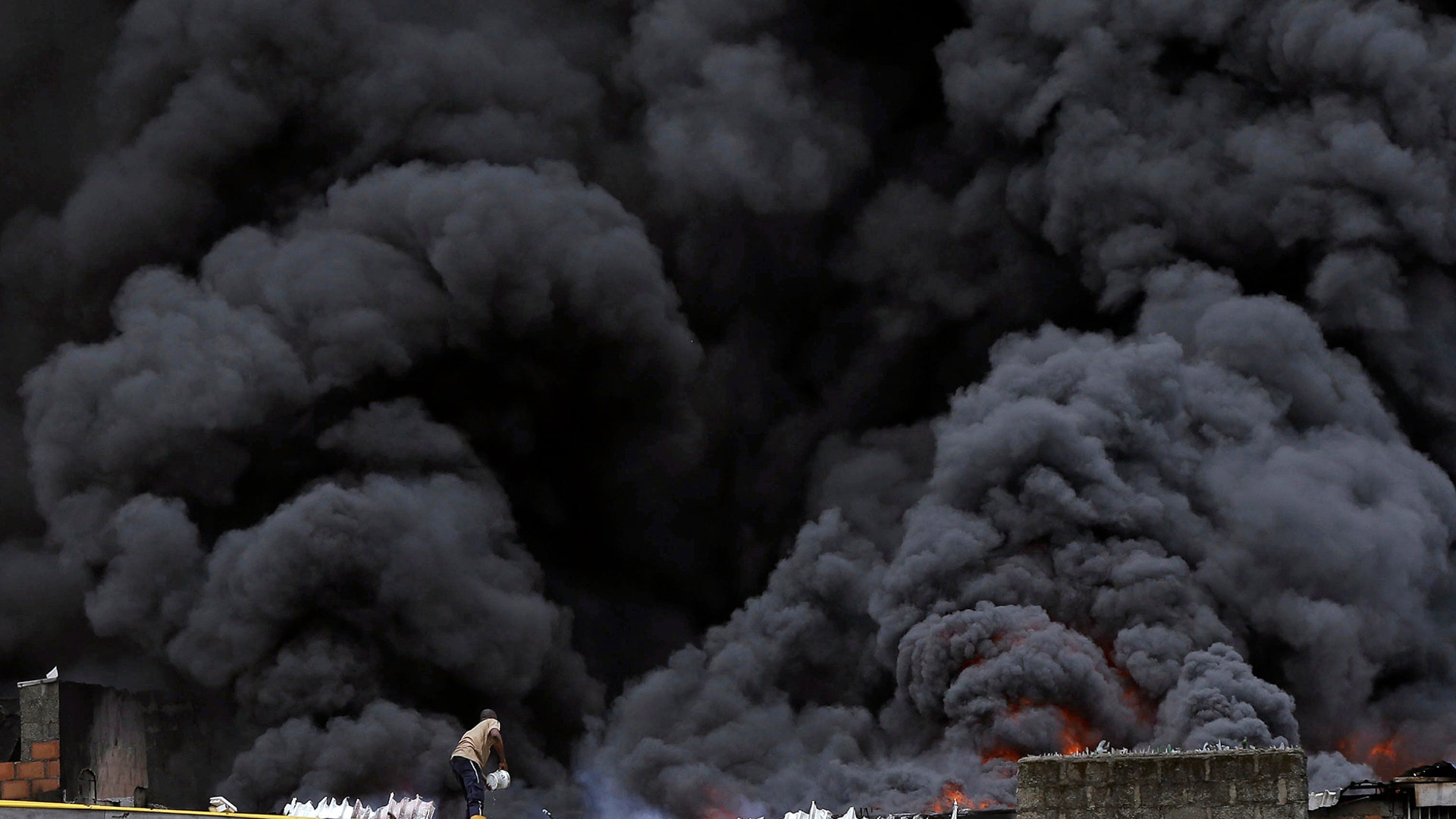A man with a bucket stands next to smoke plumes from a market fire in downtown Lagos, Nigeria, Nov. 5, 2019.