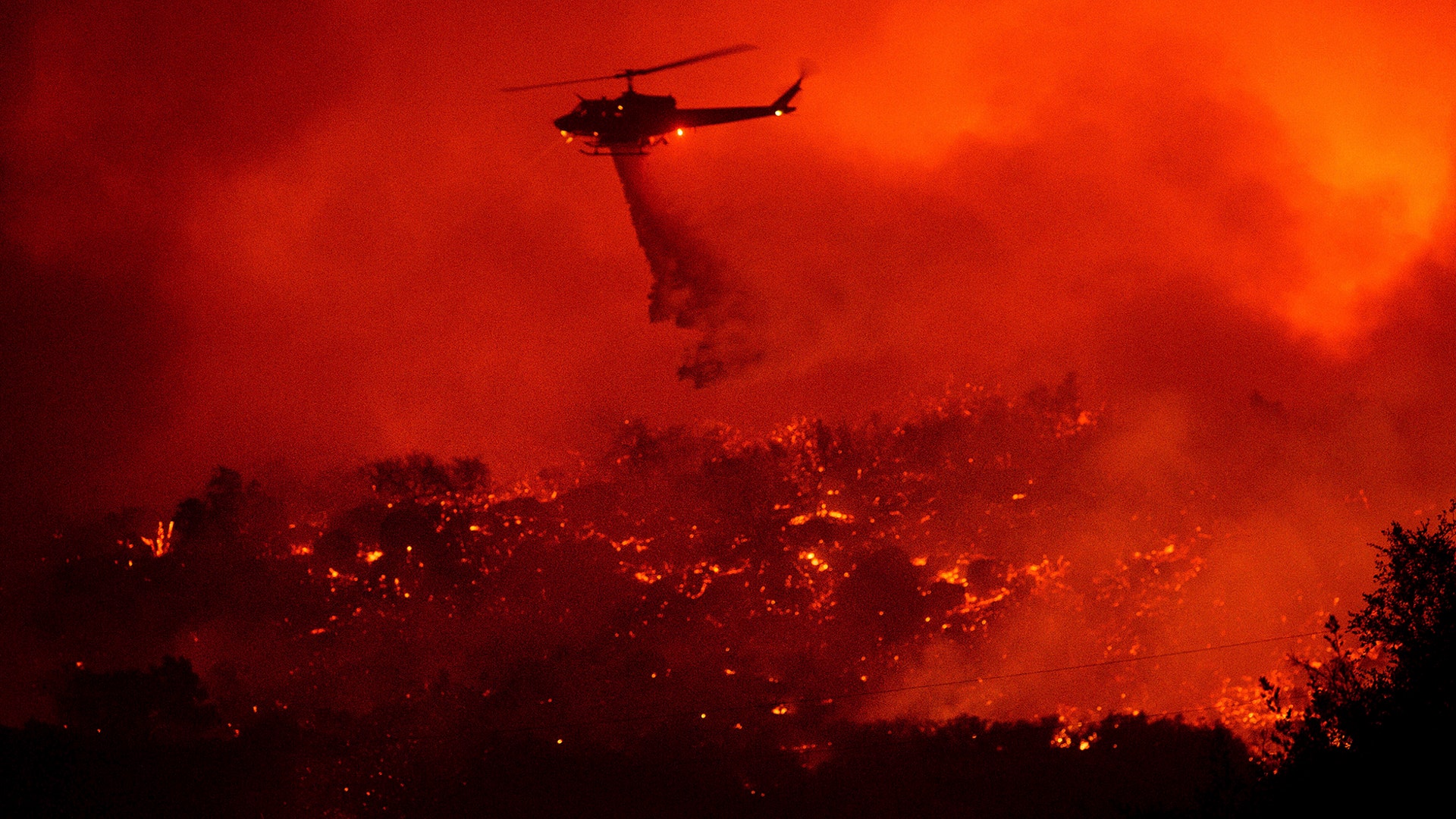 A helicopter drops water on the Cave Fire burning along Highway 154 in Los Padres National Forest above Santa Barbara, Calif., Nov. 26, 2019.