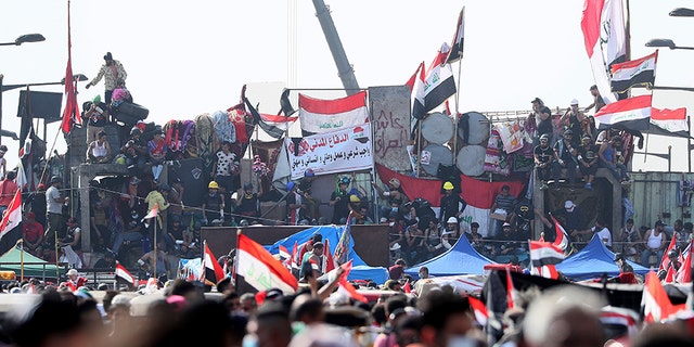 Anti-government protesters stand on barriers set by Iraqi security forces to close a bridge leading to the Green Zone government areas during ongoing protests in Baghdad, Iraq, on Monday.