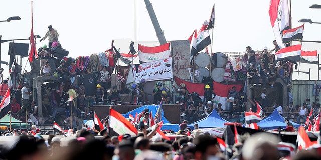 Anti-government protesters stand on barriers set by Iraqi security forces to close a bridge leading to the Green Zone government areas during ongoing protests in Baghdad, Iraq, on Monday.