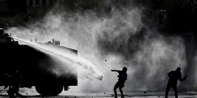 Demonstrators clash with a police water cannon during an anti-government protest in Santiago, Tuesday, Nov. 5, 2019. Chileans have been taking to the streets and clashing with the police to demand better social services and an end to economic inequality, even as the government announced that weeks of demonstrations are hurting the country's economic growth. (AP Photo/Esteban Felix)