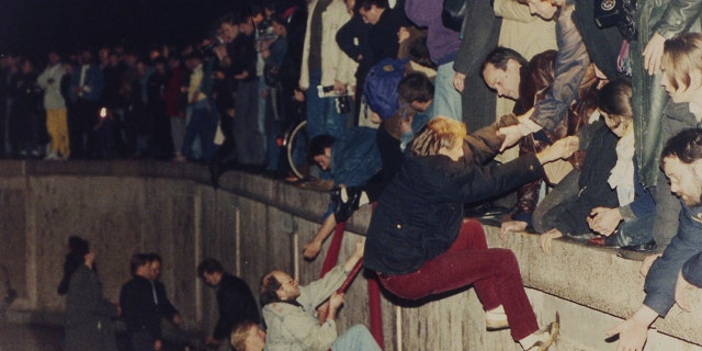 People climbing the Berlin Wall which had divided the city since the end of World War II, near the Brandenburg Gate, on Nov. 10, 1989. (AP Photo/Jockel Finck, File)