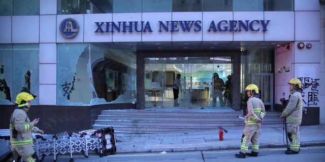 Firefighters stand outside the offices of China's Xinhua News Agency after its windows were shattered during protests in Hong Kong, Saturday, Nov. 2, 2019. 