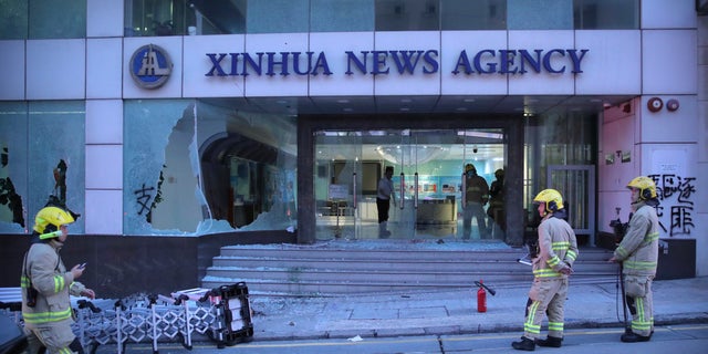 Firefighters stand outside the offices of China's Xinhua News Agency after its windows were shattered during protests in Hong Kong, Saturday, Nov. 2, 2019. 