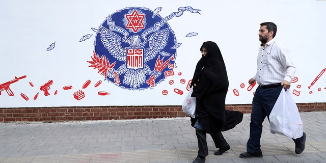 People walk past a satirical drawing of the Great Seal of the United States after new anti-U.S. murals on the walls of former U.S. embassy unveiled in a ceremony in Tehran, Iran, Saturday, Nov. 2, 2019. (AP Photo/Vahid Salemi)