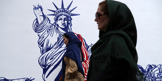 People walk past a satirical drawing of Statue of Liberty after new anti-U.S. murals on the walls of former U.S. embassy unveiled in a ceremony in Tehran, Iran, Saturday, Nov. 2, 2019. (AP Photo/Vahid Salemi)