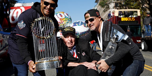 Washington Nationals manager Dave Martinez, left, and general manager Mike Rizzo, right, pose with Sidney Walton, age 100, after showing him the World Series and NLCS trophies before a parade to celebrate the team's World Series baseball championship over the Houston Astros, Saturday, Nov. 2, 2019, in Washington. (AP Photo/Patrick Semansky)