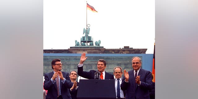 In this on Friday, June 12, 1987 file photo, U.S. President Ronald Reagan acknowledges the applause after speaking to an audience in front of the Brandenburg Gate in Berlin. Beside Reagan are the President of the German Parliament Philipp Jenninger, left, and Germany's Chancellor Helmut Kohl, right.