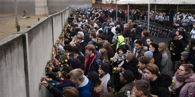 Young people stuck flowers in remains of the Berlin Wall during a commemoration ceremony to celebrate the 30th anniversary of the fall of the Berlin Wall at the Wall memorial site at Bernauer Strasse in Berlin, Saturday, Nov. 9, 2019. 