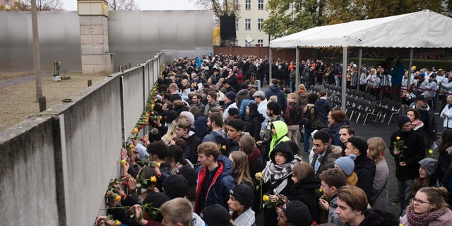 Young people stuck flowers in remains of the Berlin Wall during a commemoration ceremony to celebrate the 30th anniversary of the fall of the Berlin Wall at the Wall memorial site at Bernauer Strasse in Berlin, Saturday, Nov. 9, 2019.