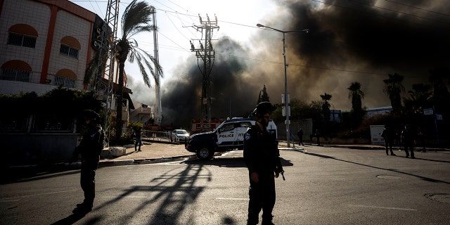 Police stands guard after a factory hit by a rocket caught fire in Sderot, southern Israel, Tuesday, Nov. 12, 2019. (AP Photo/Tsafrir Abayov)