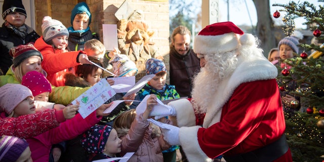 A man dressed as Santa Claus is welcomed by children during the opening of the most famous German Christmas mail office in the small village of Himmelpfort north of Berlin, Germany. (Soeren Stache/dpa via AP)