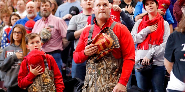 A man and boy dressed in chest waders holding their hats to their hearts during the Pledge of Allegiance at the start of the rally Thursday. (AP Photo/Gerald Herbert)