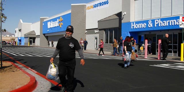 Eddie Medina, 62, carries groceries he bought for his wife at the reopening of the Cielo Vista Walmart, Thursday, Nov. 14, 2019, in El Paso, Texas. He said his wife Cecy Medina is a Walmart employee who witnessed the shooting there on Aug. 3 that left 22 people dead. He said she's still too traumatized to enter the store, and is currently in therapy paid for by Walmart. The Texas-shaped logo on his shirt read "My wife is a cancer survivor and a Walmart survivor. She is El Paso strong."