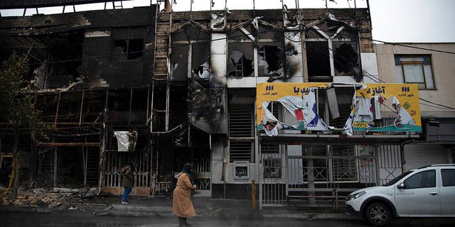 People walk past buildings that burned during protests that followed the Iran's decision to raise gasoline prices.