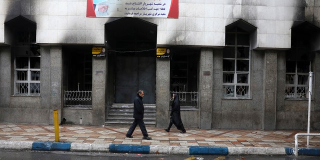 People walk past a bank that was burned during recent protests, in Shahriar, Iran, some 40 kilometers (25 miles) southwest of the capital, Tehran, Wednesday, Nov. 20, 2019. Protests over government-set gasoline prices rising struck at least 100 cities and towns, spiraling into violence that saw banks, stores and police stations attacked and burned.