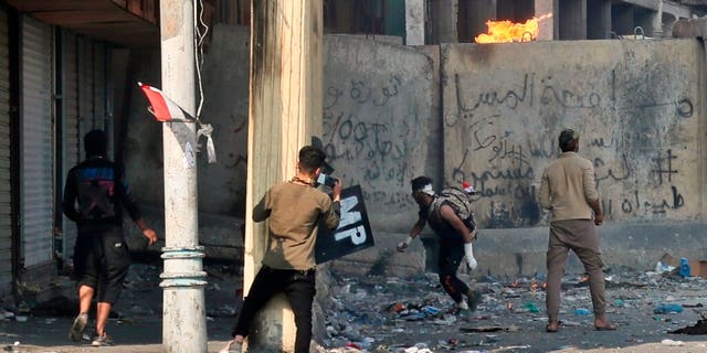Anti-government protesters throw a Molotov cocktail toward riot police during clashes in Baghdad.