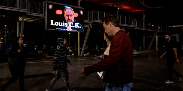 In this Thursday, Nov. 28, 2019 photo, Israelis walk past a billboard showing Comedian Louis C.K. in the Israeli city of Holon near Tel Aviv. (AP Photo/Tsafrir Abayov)