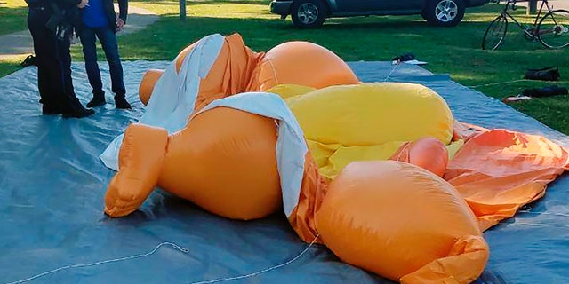 A responding officer and an unidentified man stand by the deflated Baby Trump at Monnish in Tuscaloosa, Ala. (Stephanie Taylor/The Tuscaloosa News via AP)