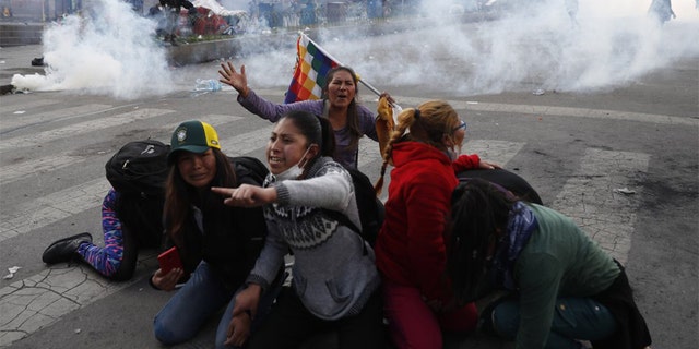 Supporter of former President Evo Morales protect themselves from tear gas launched by the police, in La Paz, Bolivia, Friday, Nov. 15, 2019. Bolivia's new interim president Jeanine Anez faces the challenge of stabilizing the nation and organizing national elections within three months at a time of political disputes that pushed Morales to fly off to self-exile in Mexico after 14 years in power. (AP Photo/Natacha Pisarenko)