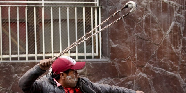 A supporter of former President Evo Morales throws a stone to police, in La Paz, Bolivia, Friday, Nov. 15, 2019. Bolivia's new interim president Jeanine Anez faces the challenge of stabilizing the nation and organizing national elections within three months at a time of political disputes that pushed Morales to fly off to self-exile in Mexico after 14 years in power. (AP Photo/Natacha Pisarenko)