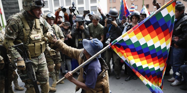 A backer of former President Evo Morales kneels in front of soldiers guarding a street in downtown La Paz, Bolivia, Friday, Nov. 15, 2019. Bolivia's new interim president Jeanine Anez faces the challenge of stabilizing the nation and organizing national elections within three months at a time of political disputes that pushed Morales to fly off to self-exile in Mexico after 14 years in power. (AP Photo/Natacha Pisarenko)