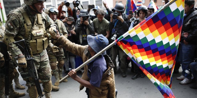 A backer of former President Evo Morales kneels in front of soldiers guarding a street in downtown La Paz, Bolivia, Friday, Nov. 15, 2019. Bolivia's new interim president Jeanine Anez faces the challenge of stabilizing the nation and organizing national elections within three months at a time of political disputes that pushed Morales to fly off to self-exile in Mexico after 14 years in power. (AP Photo/Natacha Pisarenko)