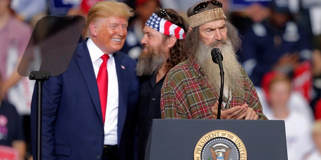 President Donald laughs with Willie Robertson, of the reality TV series Duck Dynasty, and Phil Roberston, the family patriarch, right, at a campaign rally in Monroe, La., Wednesday, Nov. 6, 2019.
