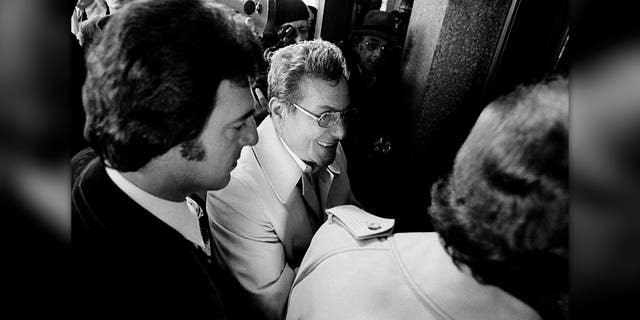 Salvatore Briguglio, center, smiles as he waits to enter the lobby of the Oakland County Jail in Pontiac, Mich., Dec. 6, 1975 where he was to appear in a court ordered lineup in connection with the disappearance of James R. Hoffa. Thomas Andretta, left, was also to appear in the lineup. (AP Photo)