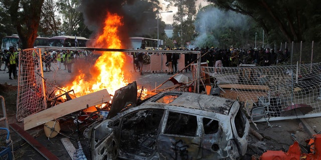 Students stand near a charred vehicle during a face-off with riot police at the Chinese University in Hong Kong, Tuesday, Nov. 12, 2019.