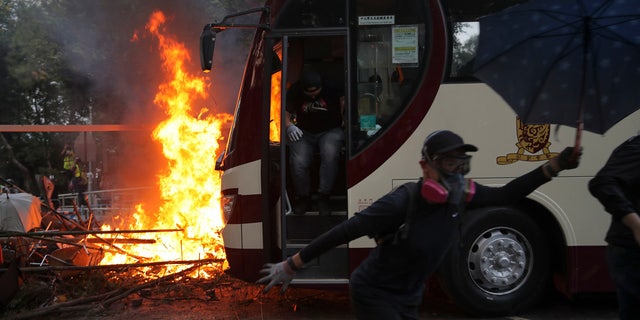 Students run past fire set near a bus during a face-off with riot police at the Chinese University in Hong Kong, Tuesday, Nov. 12, 2019.