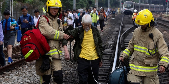 Firefighters help an elderly woman as commuters walk on the railway after their train service is disrupted by pro-democracy protesters in Hong Kong, Tuesday, Nov. 12, 2019.