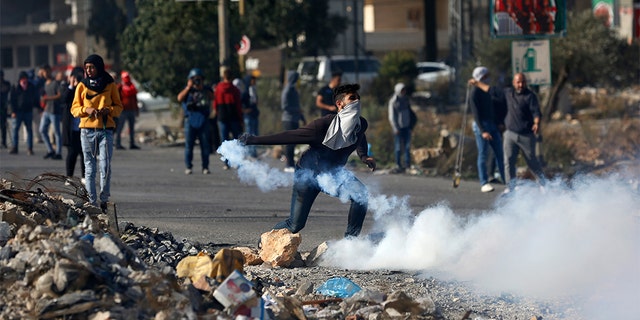 Palestinian demonstrator throws back tear gas fired by Israeli troops during the protest against the U.S. announcement that it no longer believes Israeli settlements violate international law., at checkpoint Beit El near the West Bank city of Ramallah, Tuesday, Nov. 26, 2019.
