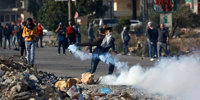 Palestinian demonstrator throws back tear gas fired by Israeli troops during the protest against the U.S. announcement that it no longer believes Israeli settlements violate international law., at checkpoint Beit El near the West Bank city of Ramallah, Tuesday, Nov. 26, 2019.