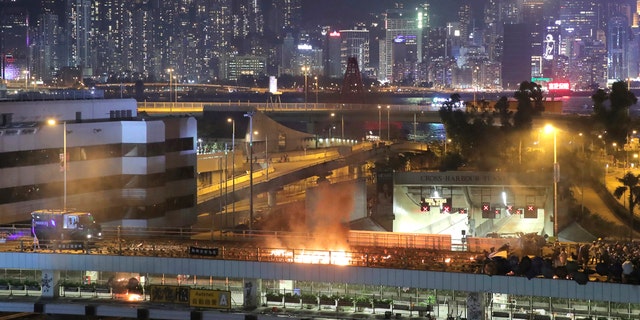 An armored police vehicle, left, approaches a burning barricade built by protestors near the entrance to the Cross Harbour Tunnel in Hong Kong, Sunday, Nov. 17, 2019.