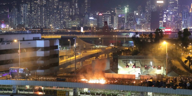 An armored police vehicle, left, approaches a burning barricade built by protestors near the entrance to the Cross Harbour Tunnel in Hong Kong, Sunday, Nov. 17, 2019.