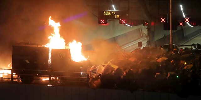 An armored police vehicle catches fire after being hit by molotov cocktails thrown by protestors, at right, on a bridge over a highway leading to the Cross Harbour Tunnel in Hong Kong, Sunday, Nov. 17, 2019.