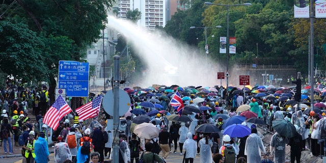 Protesters hold American flags as an armored police vehicle sprays water during a confrontation near the Hong Kong Polytechnic University in Hong Kong, Sunday, Nov. 17, 2019.