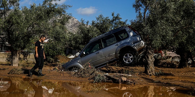 A man walks past a car moved by the force of flood water after storms in Kineta village, about 42 miles west of Athens, on Monday. (AP)