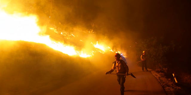 Firefighters walks on a road leading to a residence as the Maria Fire burns on a hillside Thursday, Oct. 31, 2019, in Somis, Calif. (AP Photo/Marcio Jose Sanchez)