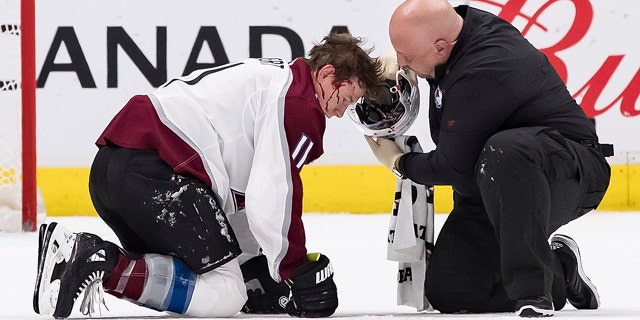 A trainer removes the helmet of Colorado Avalanche's Matt Calvert after Calvert was struck by the puck while blocking a Vancouver Canucks shot during the third period of an NHL hockey game Saturday, Nov. 16, 2019, in Vancouver, British Columbia. (Darryl Dyck/The Canadian Press via AP)