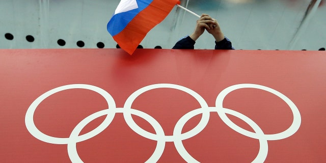 FILE - In this Feb. 18, 2014, file photo, a Russian flag is held above the Olympic Rings at Adler Arena Skating Center during the Winter Olympics in Sochi, Russia. A World Anti-Doping Agency (WADA) panel on Monday Nov. 25, 2019, has recommended Russian athletes be forced to compete as neutrals at the 2020 Olympics in Tokyo and other major upcoming events. (AP Photo/David J. Phillip, File)