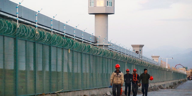 FILE PHOTO: Workers walk by the perimeter fence of what is officially known as a vocational skills education centre in Dabancheng in Xinjiang Uighur Autonomous Region, China September 4, 2018. This centre, situated between regional capital Urumqi and tourist spot Turpan, is among the largest known ones, and was still undergoing extensive construction and expansion at the time the photo was taken. Picture taken September 4, 2018. REUTERS/Thomas Peter/File Photo - RC112C876810