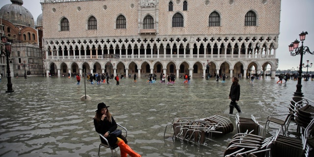 A woman sits in a chair in a flooded St. Mark's Square, in Venice, Wednesday, Nov. 13, 2019.