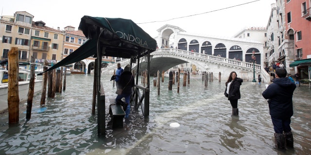 Tourists take pictures in front of the Rialto Bridge while wading through high water, in Venice, Wednesday, Nov. 13, 2019.