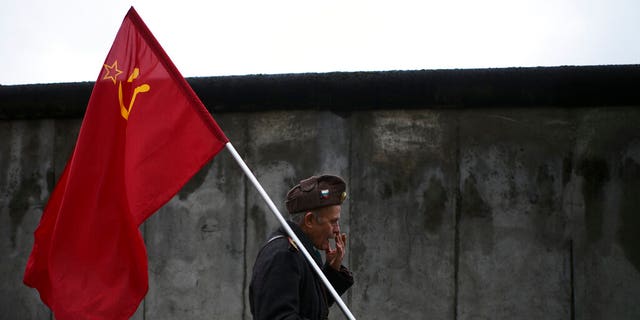 An elderly man with a Soviet flag walks in front of remains of the Berlin Wall after commemorations celebrating the 30th anniversary of the fall of the Berlin Wall at the Wall memorial site at Bernauer Strasse in Berlin, Saturday, Nov. 9, 2019. The man, who would not give his name, walks around with the flag as a protest against capitalism.