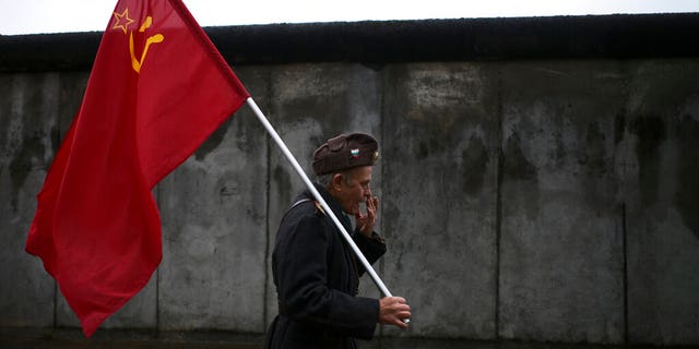 An elderly man with a Soviet flag walks in front of remains of the Berlin Wall after commemorations celebrating the 30th anniversary of the fall of the Berlin Wall at the Wall memorial site at Bernauer Strasse in Berlin, Saturday, Nov. 9, 2019. The man, who would not give his name, walks around with the flag as a protest against capitalism.