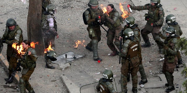 Police officers run to get assistance after being hit with a gasoline bomb thrown by protesters during an anti-government protest in Santiago, Chile, Monday, Nov. 4, 2019. 