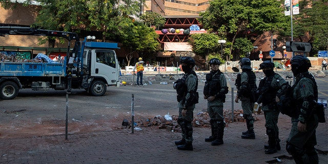 Police officers watch as workers clear the road in front of the Polytechnic University in Hong Kong on Wednesday.