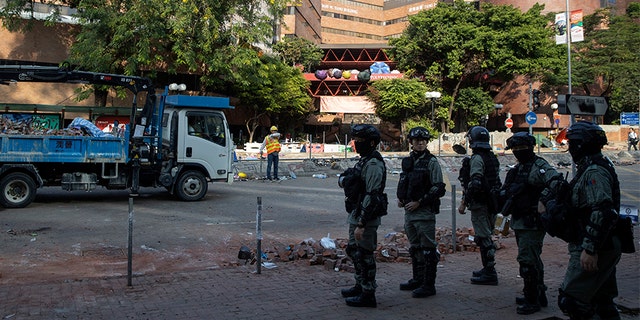 Police officers watch as workers clear the road in front of the Polytechnic University in Hong Kong on Wednesday.